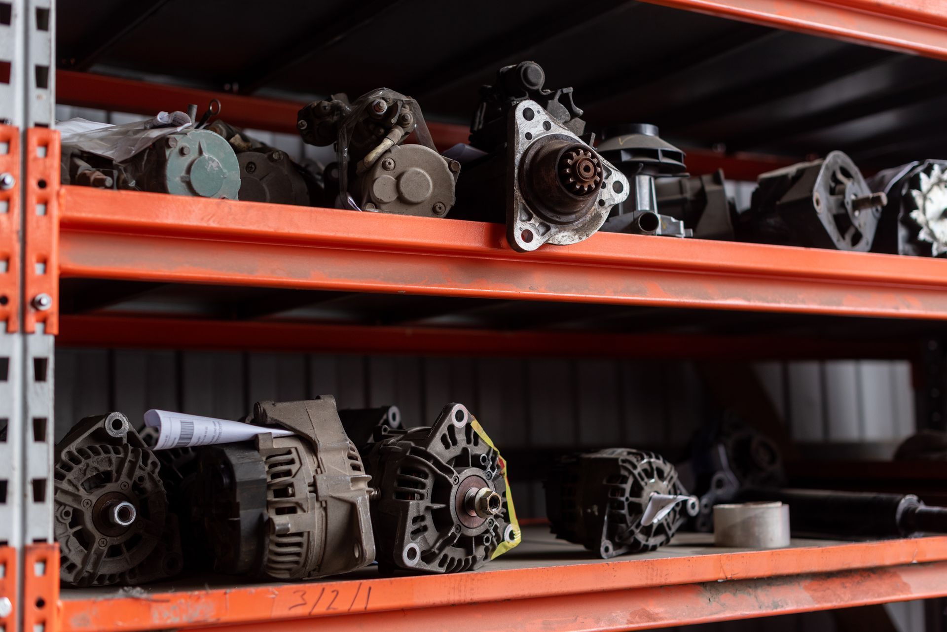 Used auto parts organized on metal shelves, including alternators and other engine components. Used auto parts organized on metal shelves, including alternators and other engine components.