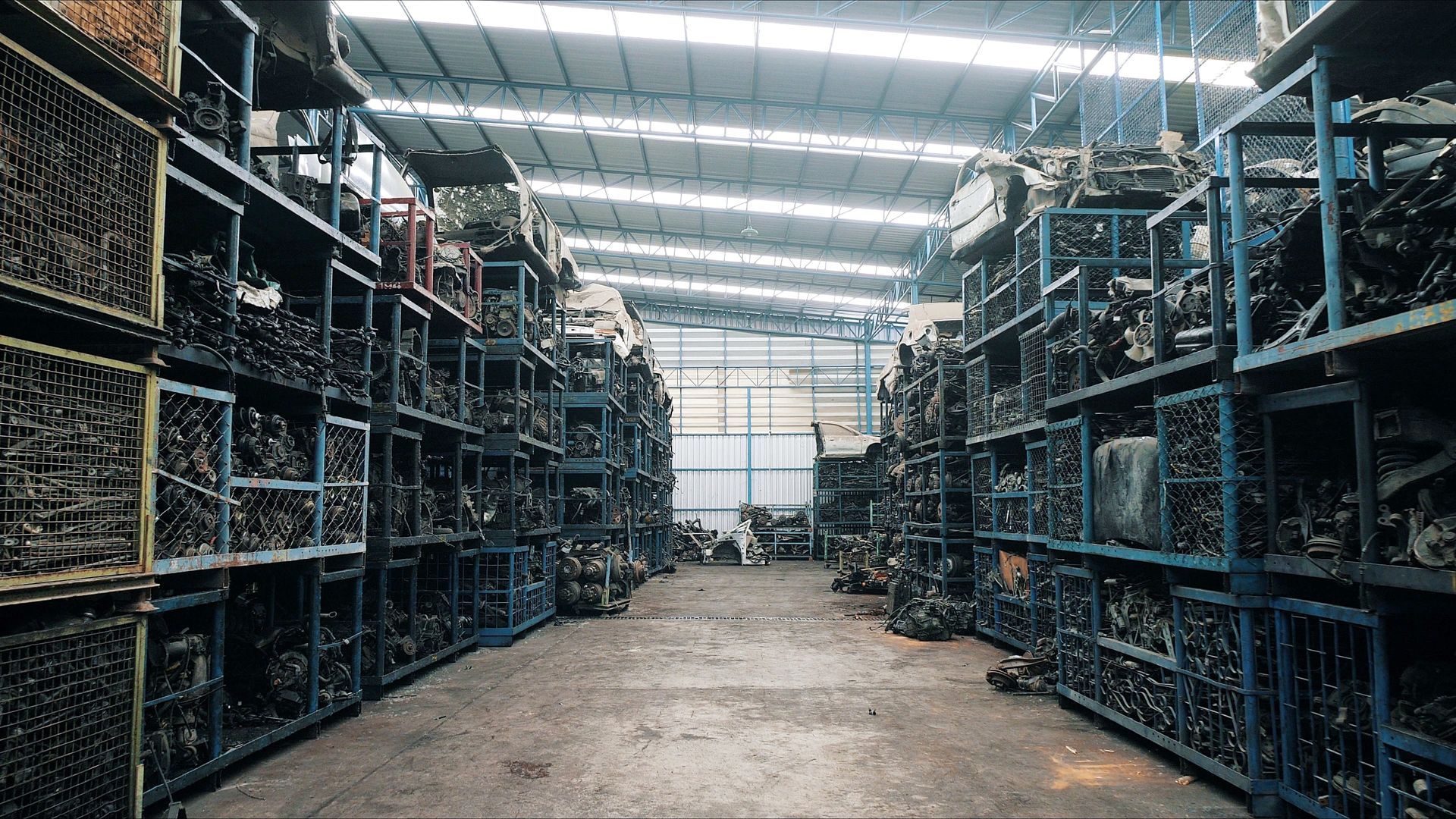 A vast warehouse aisle lined with metal shelving units filled with various stacked automotive spare parts.