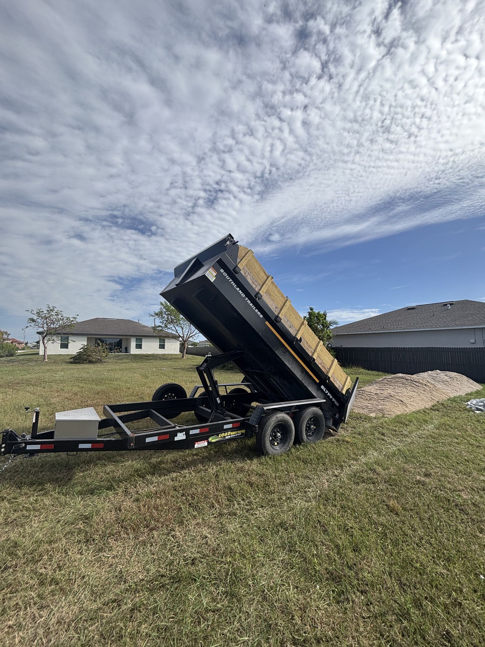 A dump truck is sitting on top of a trailer in a grassy field.