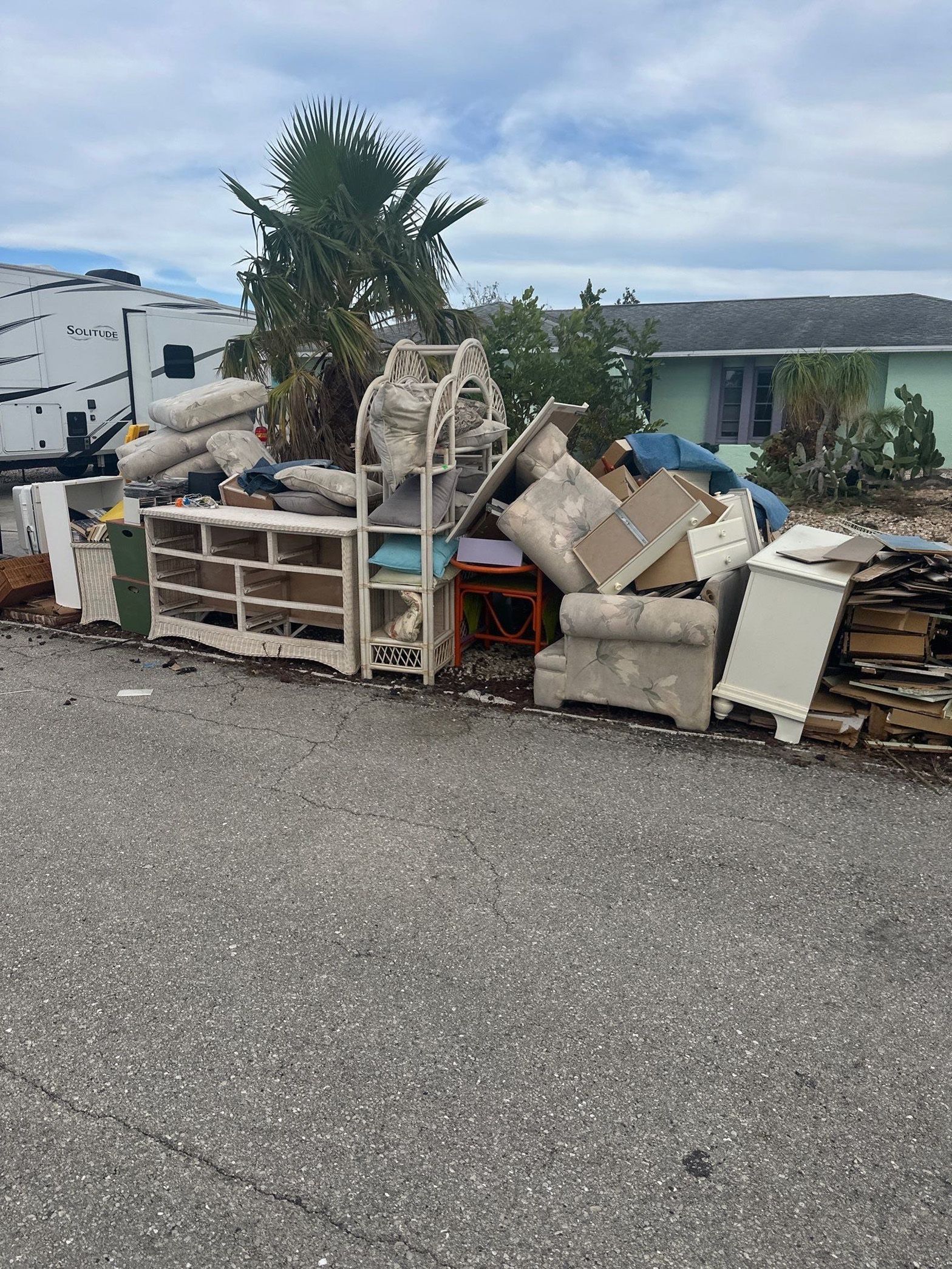A pile of furniture is sitting in a gravel lot in front of a house.