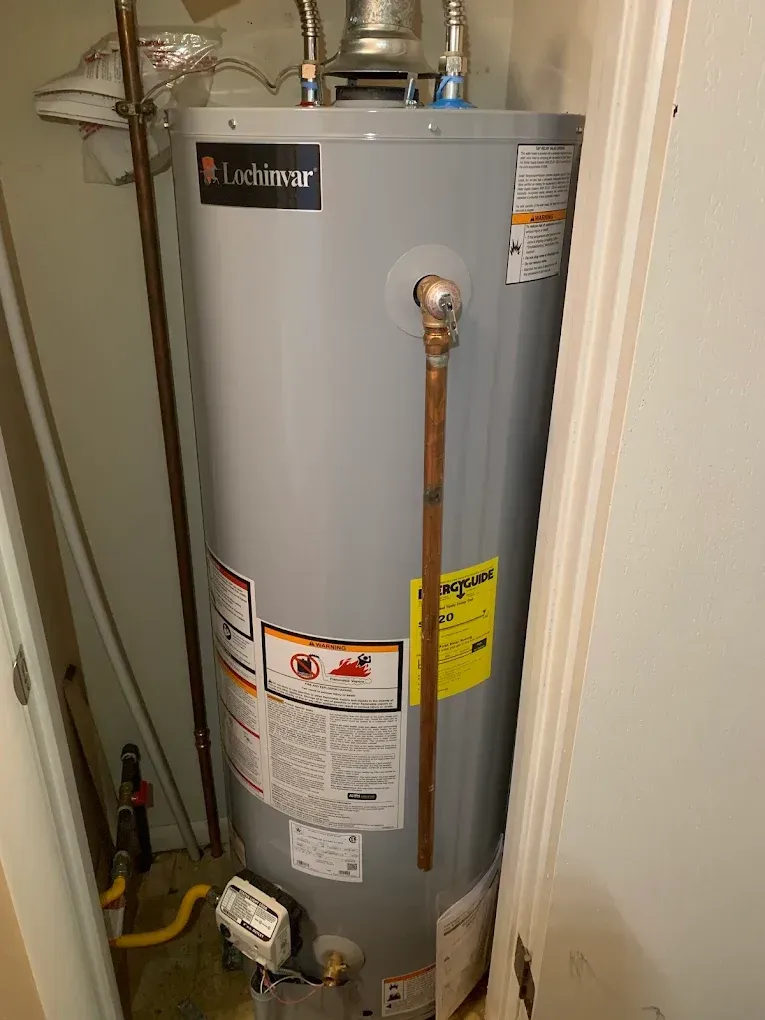 A water heater in a closet, with copper pipes and a gas line.
