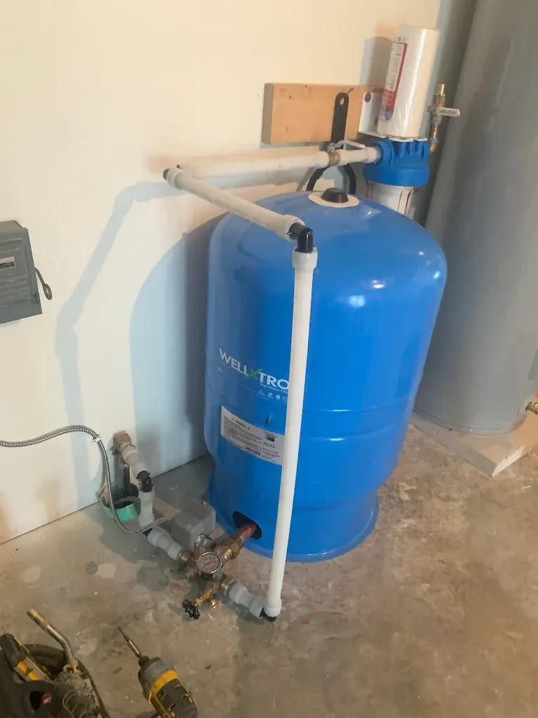 Blue well water pressure tank with white pipes and water filter attached, in a utility room.