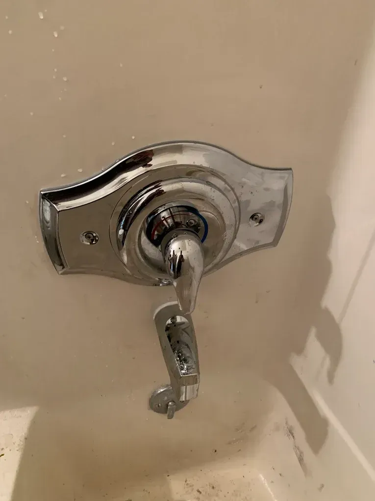 Chrome bathtub faucet with attached handle, mounted on a white wall.