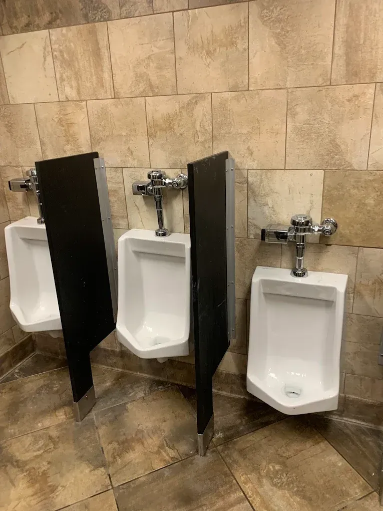Three white urinals with black dividers on a tiled wall in a restroom.