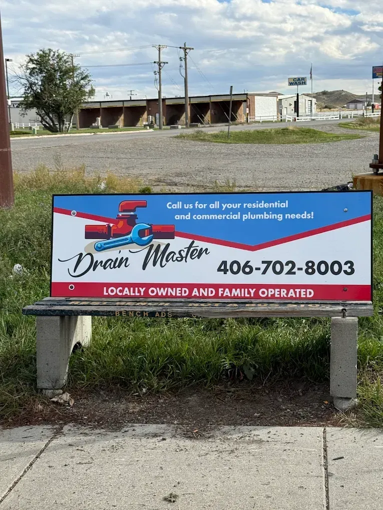 Sign for Drain Master plumbing, on a bench, with phone number, in an outdoor setting.