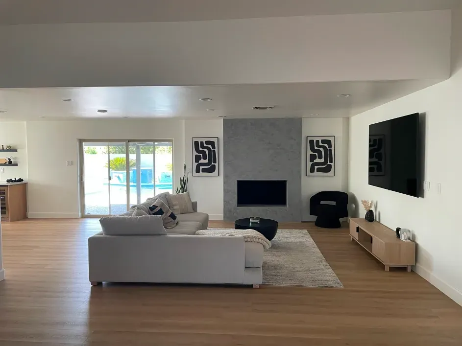 A bright living room with a gray fireplace, light wood floors, a white sofa, and a television on the wall.