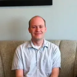 A man is sitting on a couch and smiling for the camera. A man is sitting on a couch and smiling for the camera.