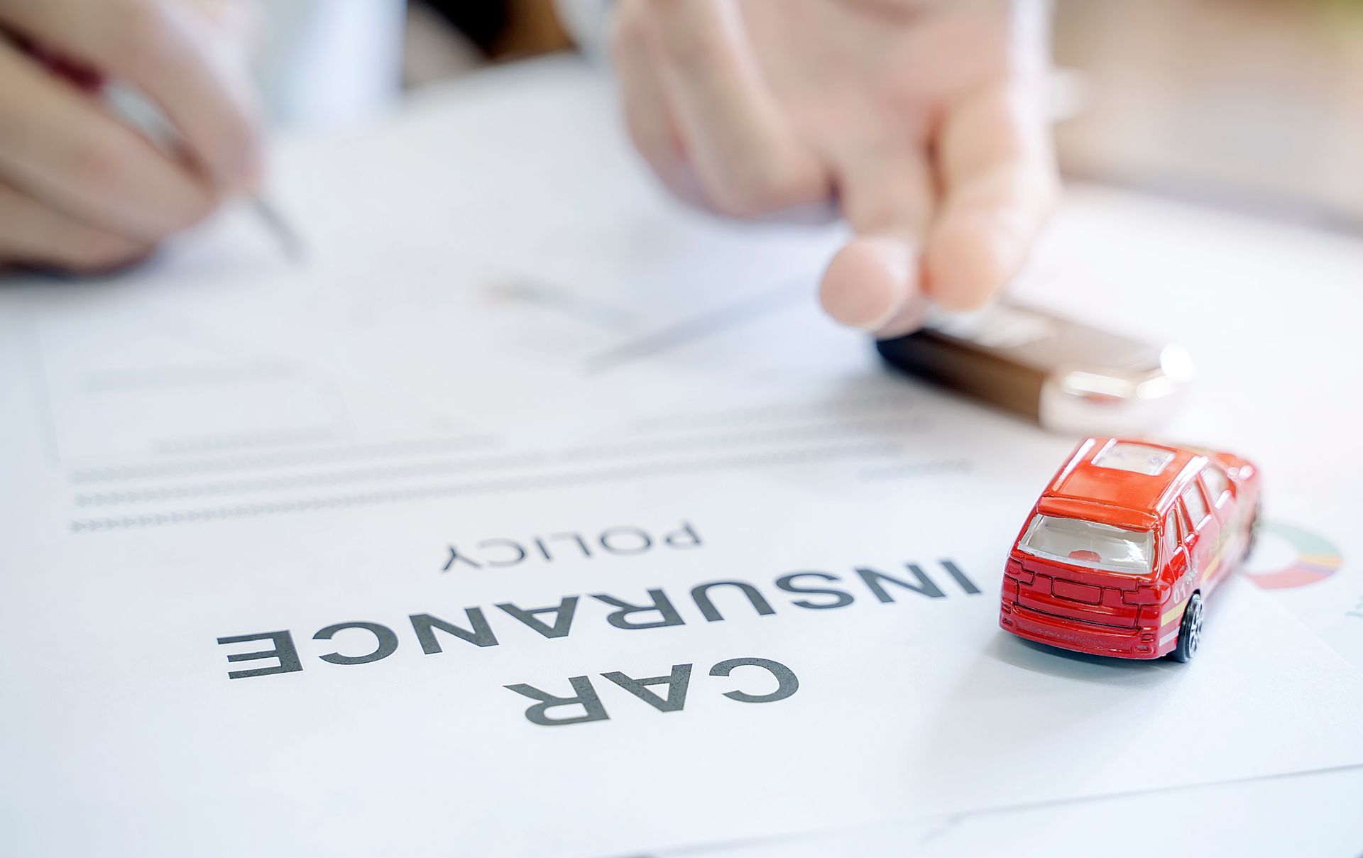 Red toy car on car insurance policy document, hand-signing the paper.
