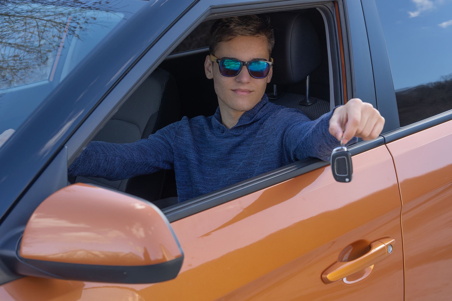 A teenager is sitting in new car and shows the key.