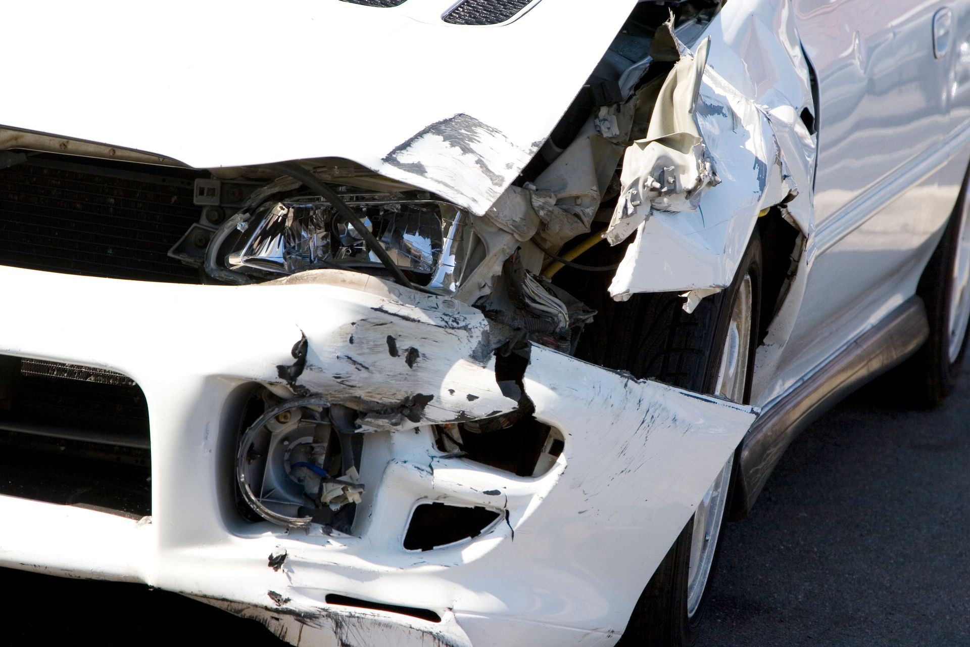 Damaged white car; front end crushed, headlight exposed, indicating a collision.