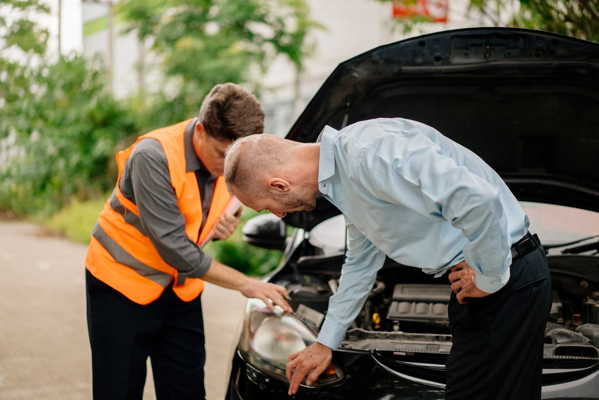 Two men inspecting a car with its hood open, pointing at the front headlight and engine area