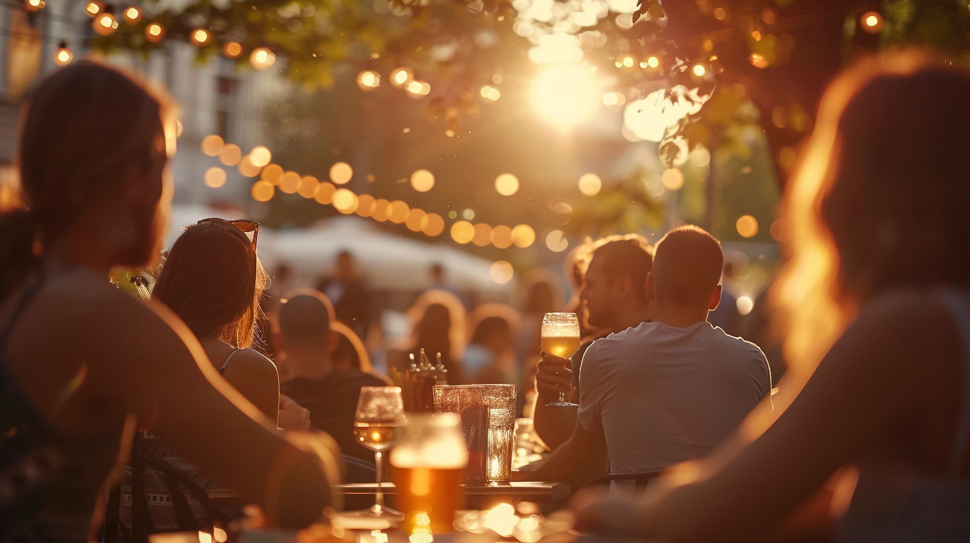 People at outdoor cafe, golden hour lighting, string lights, drinking, sunlit backdrop.