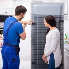 Um técnico está consertando a geladeira e a cliente está acompanhando o conserto da geladeira em casa.