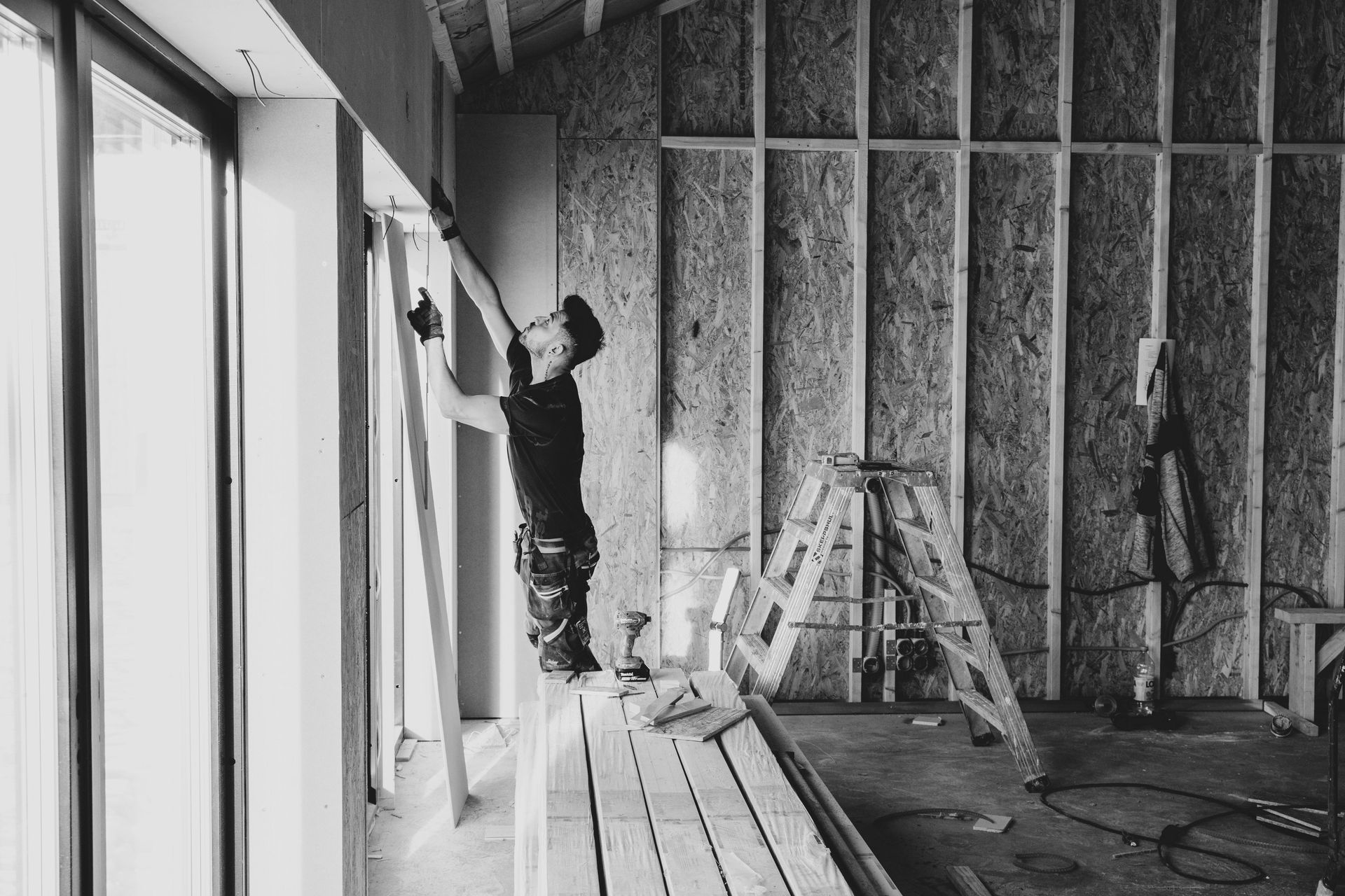 A person in a black shirt installs trim around a large glass door in a room with unfinished wooden wall framing.