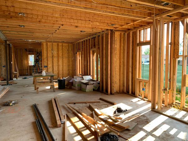A sunlit, unfinished room in a house under construction with exposed wooden wall studs, floor joists, and scattered lumber.