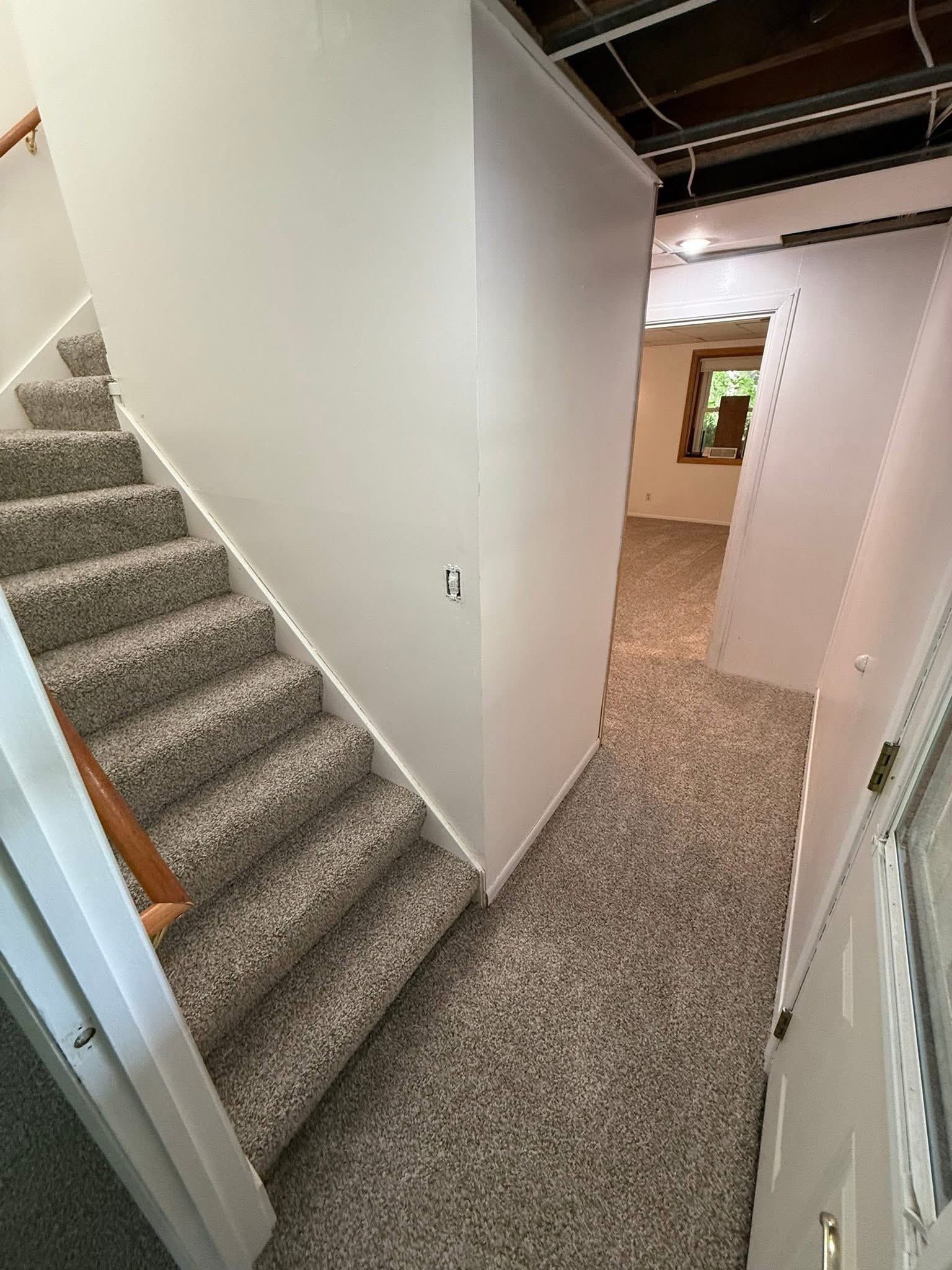 Staircase with carpet, leading up. Hallway with carpet and open doorway.