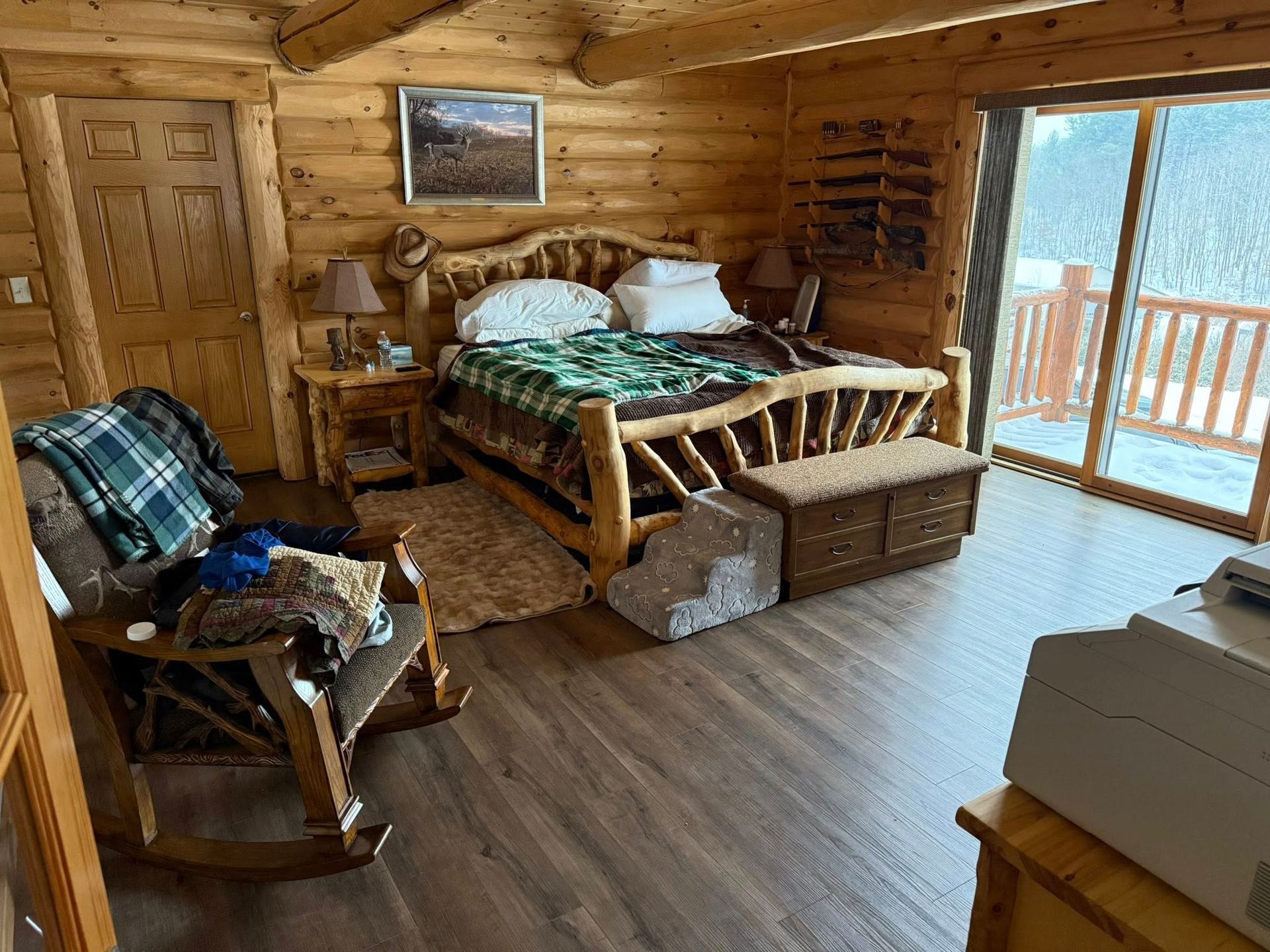Log cabin bedroom with a wooden bed, rocking chair, and a sliding door leading to a balcony.