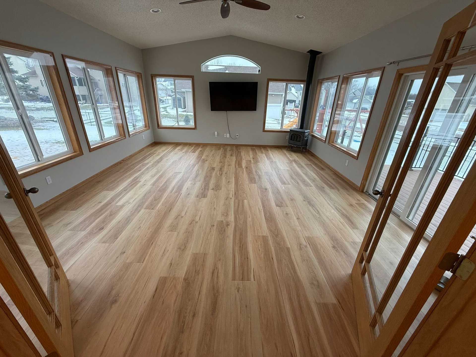 Bright, empty sunroom with wooden floors, many windows, and a black fireplace.