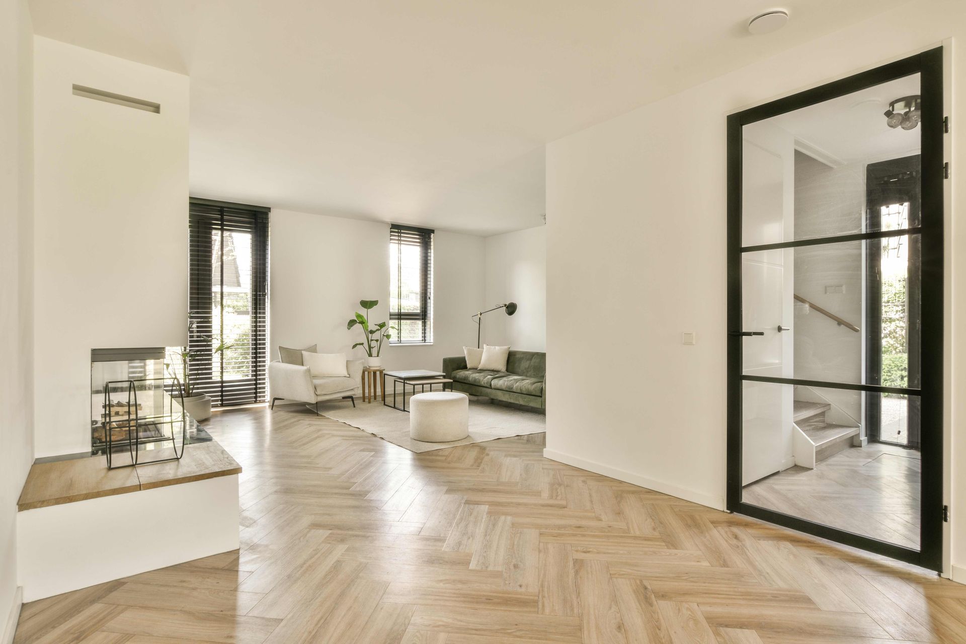 Modern living room with herringbone wood floors, white walls, and black-framed glass door.