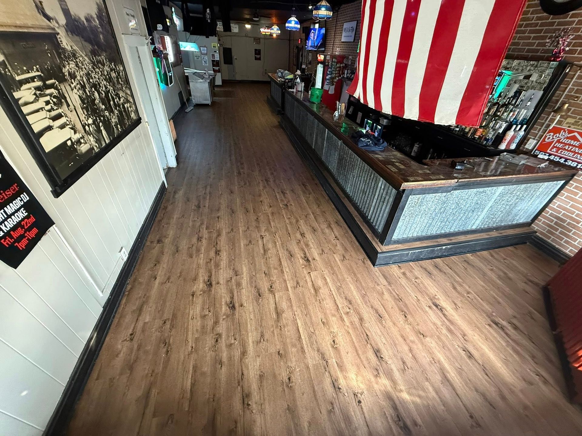 Interior view of a bar with a wooden floor, bar counter, and American flag.