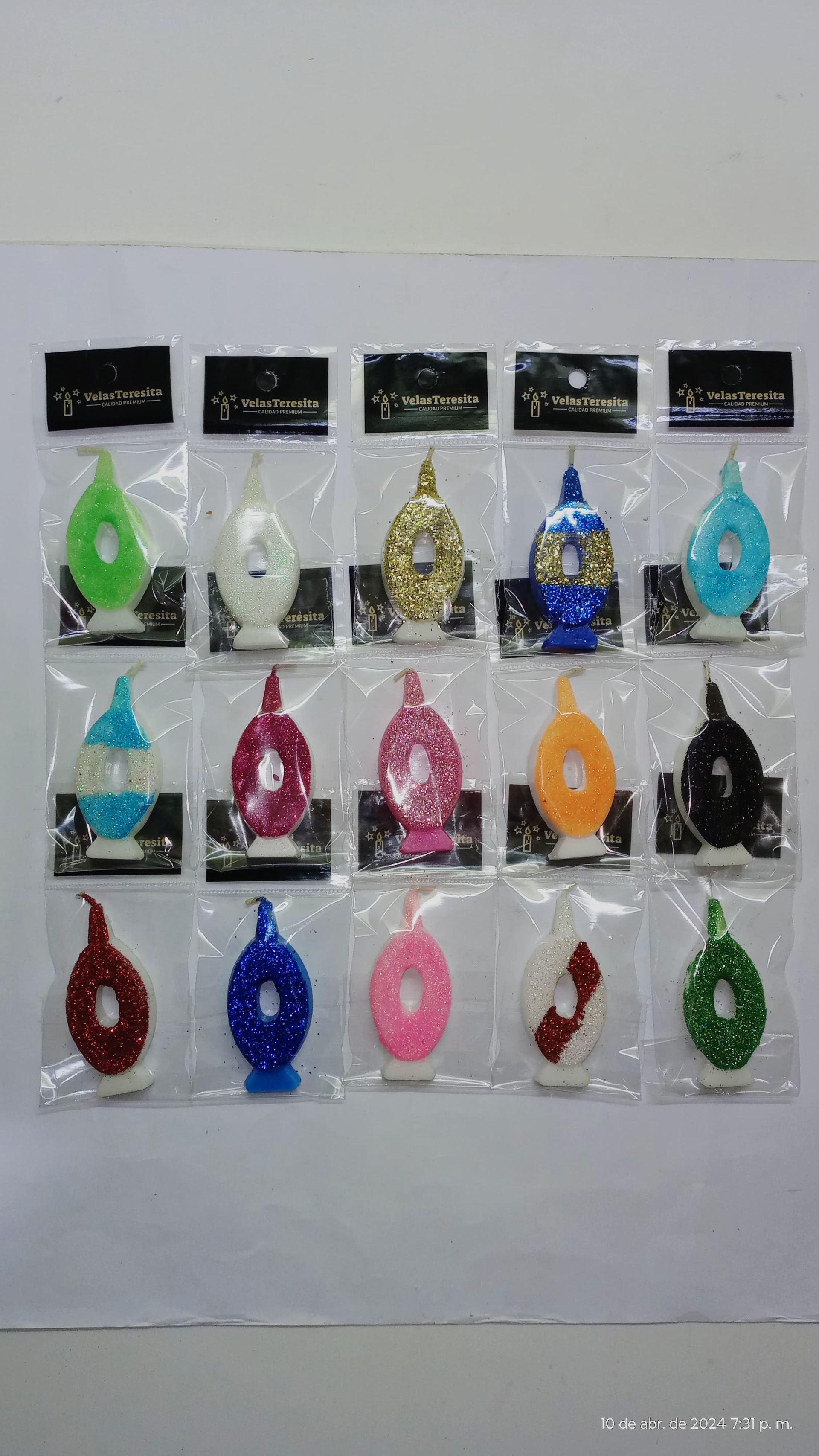 Quince velas en forma de lágrima en varios colores, cada una envuelta en plástico con etiqueta negra.