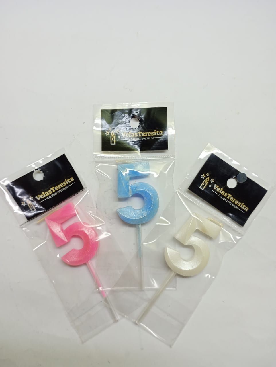 Tres velas de cumpleaños número 5 en envase de plástico: rosa, azul y blanco.