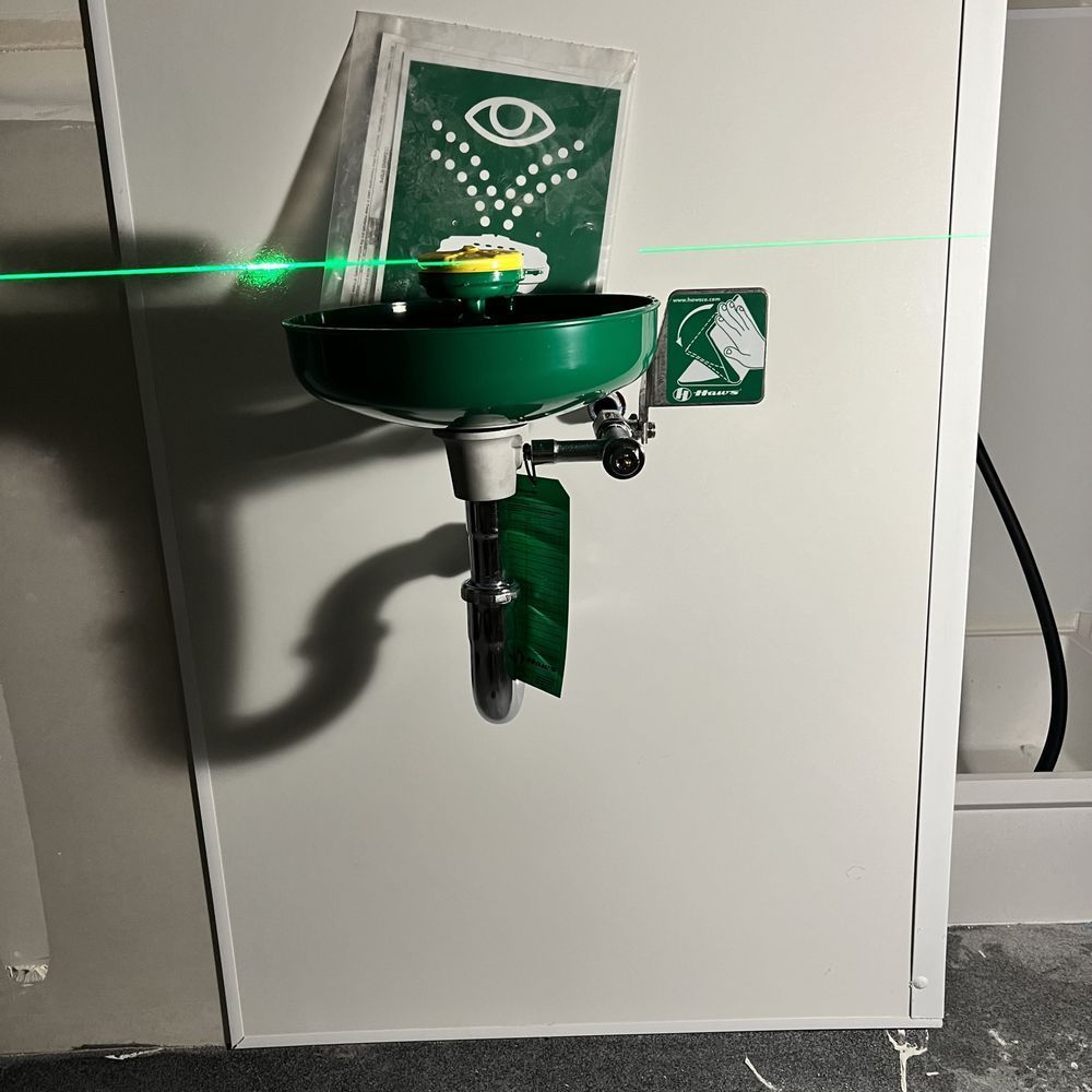 Green laser level mounted on a white cabinet, projecting a horizontal beam in a workshop.