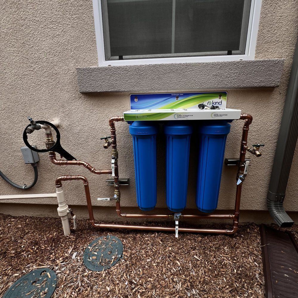 Three blue water filter canisters mounted outside beneath a window with copper pipes and valves