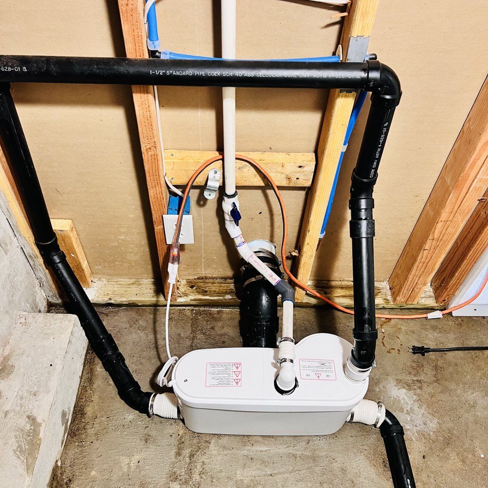 White sump pump basin with black PVC pipes and wiring in a basement utility area