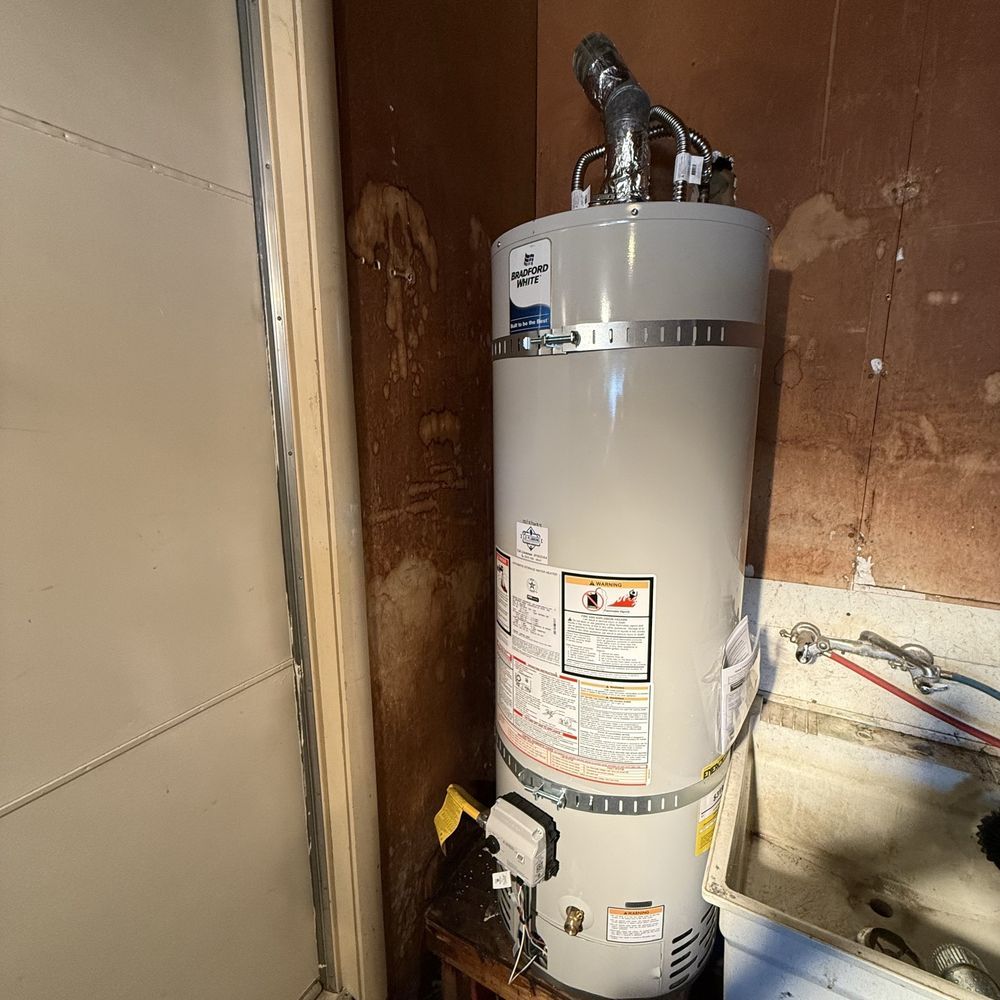 Tall white water heater in a utility closet with exposed pipes and venting.