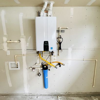 Wall-mounted white water heater with exposed pipes and valves in an unfinished laundry room