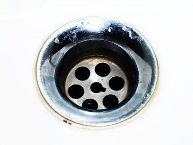 Close-up of a metal sink drain with a circular strainer and dark drain holes