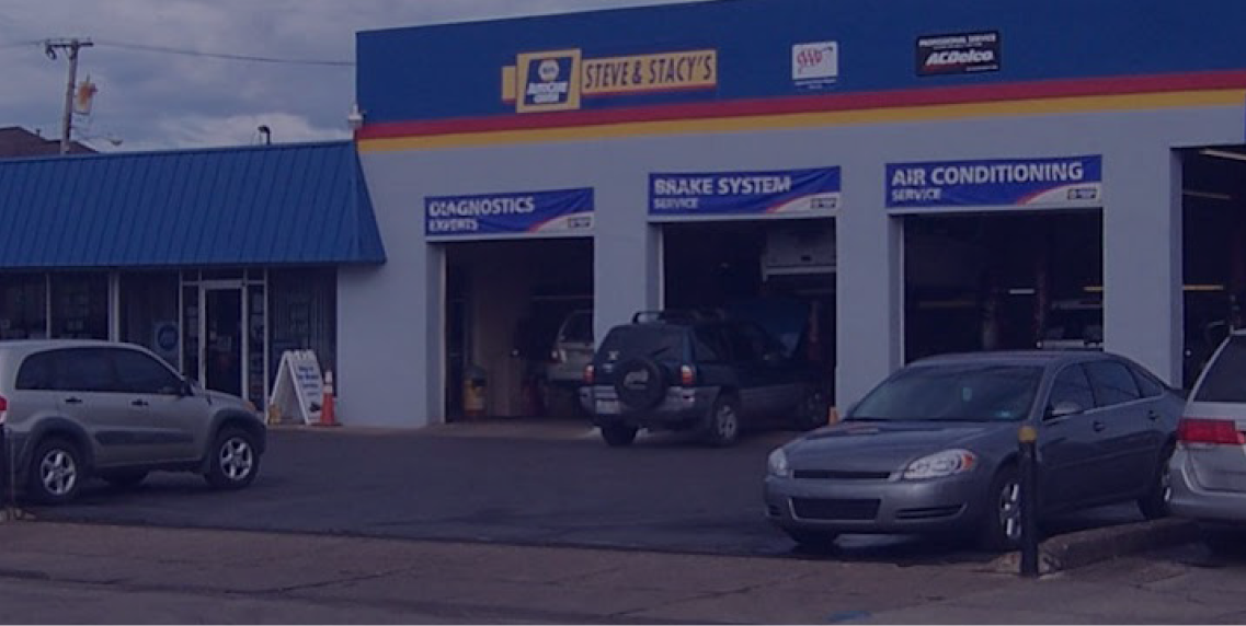 Exterior of an auto repair shop with three bays. Cars are parked in front. | Steve & Stacy's Servicenter