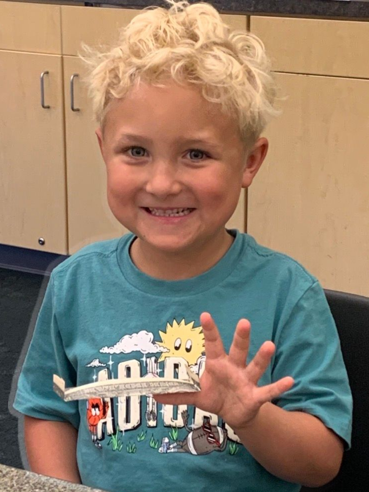 Smiling child in a teal shirt holding up four fingers in a classroom kitchen area
