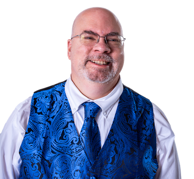 A smiling person wears a white collared shirt, blue paisley vest, and matching tie against a white background.