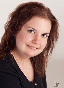 A woman with long brown hair and blue eyes is smiling for the camera.