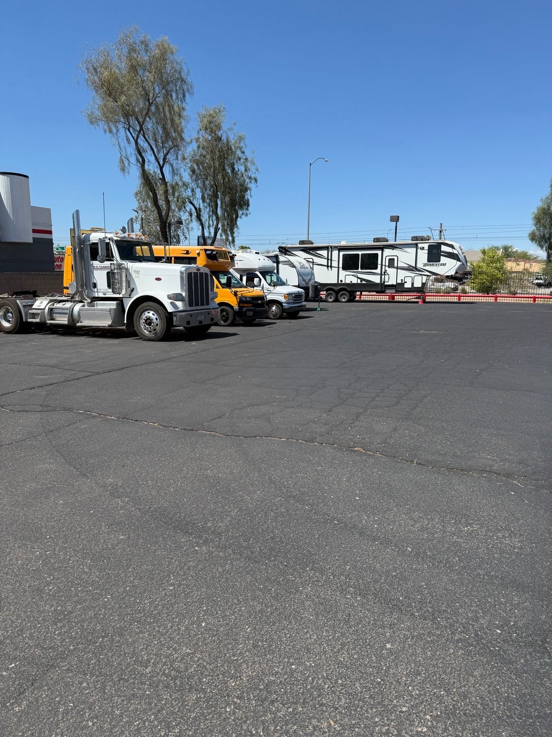 A sunny parking lot with a white truck, a yellow truck, and an RV.