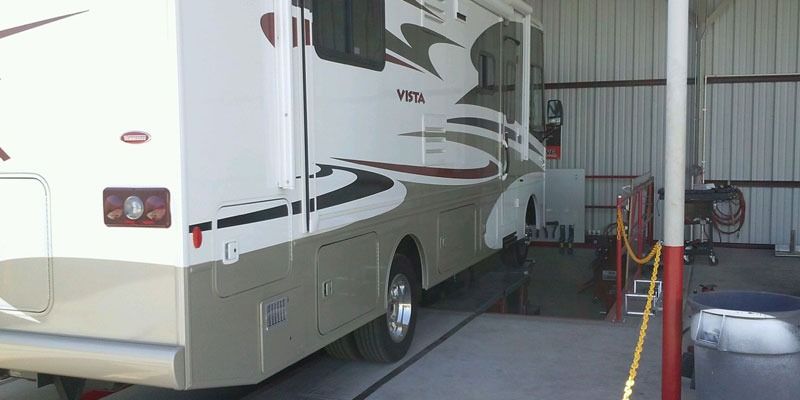 An RV parked in a garage, a wheel is being worked on.