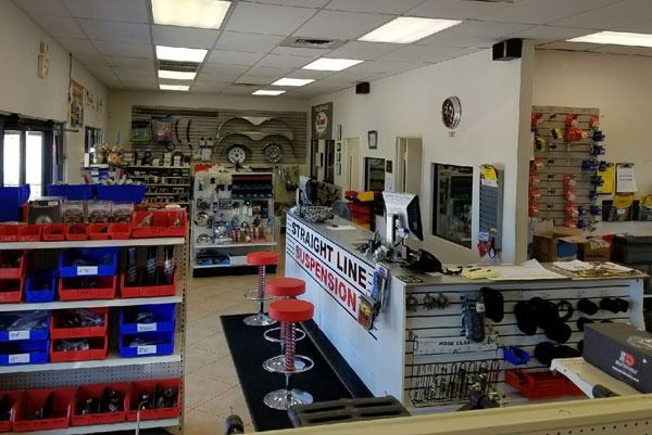 Interior of an auto parts store. Shelves with parts, red and blue bins, white counter, and a customer waiting area with stools.
