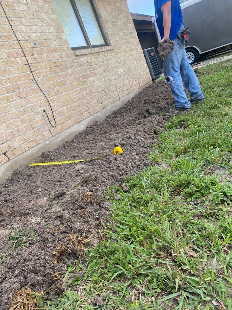 Man standing near a freshly dug flower bed next to a brick house.