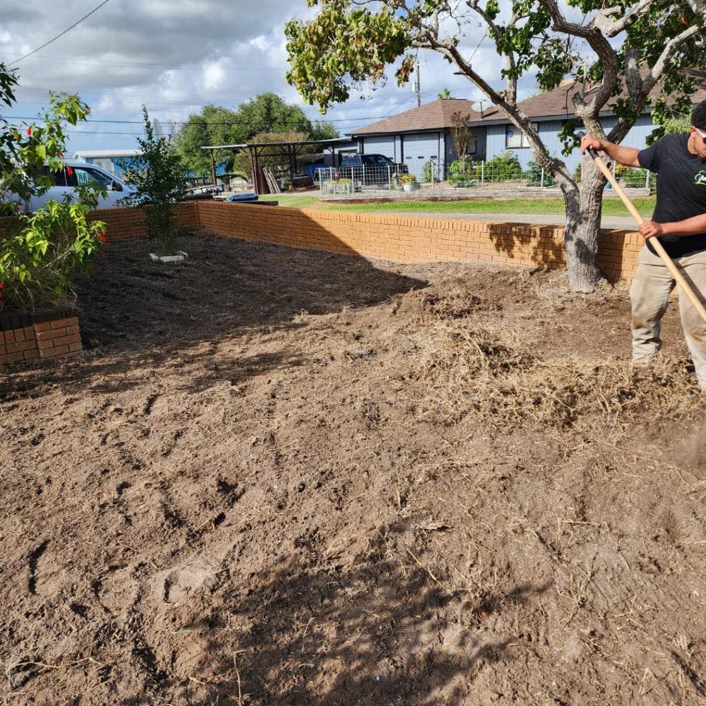 Man raking dirt in a backyard. Tan pants, black shirt. Raised bed in background, houses and sky visible.