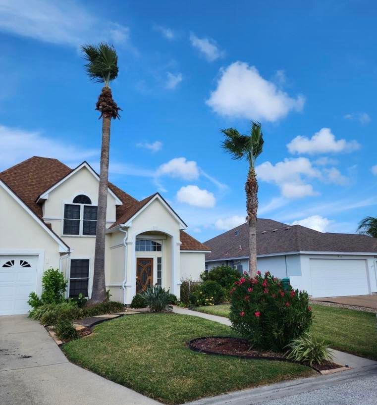 A white house with a brown roof and palm trees under a blue sky with clouds.