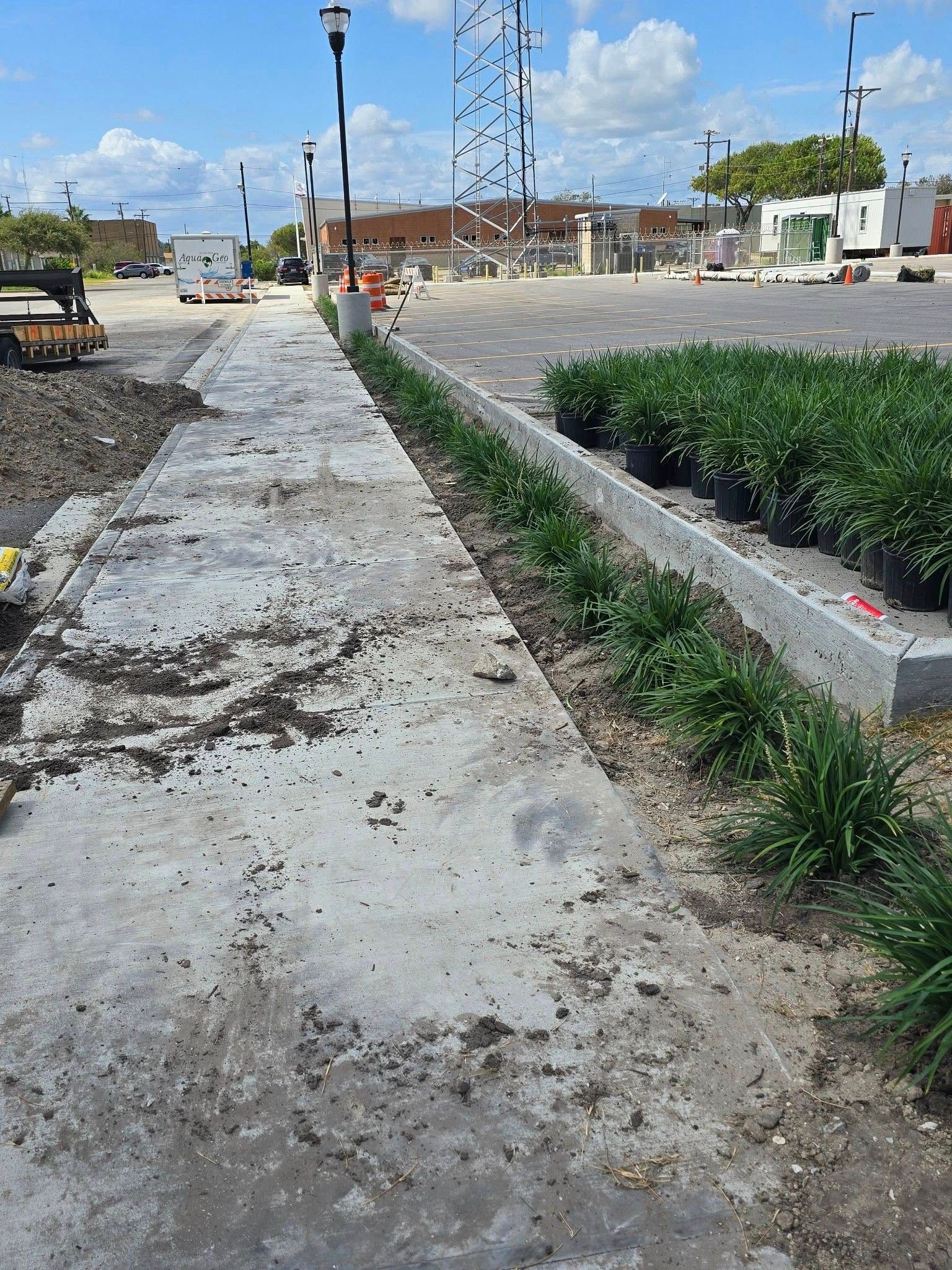 A concrete path with a narrow planting bed, and a building and sky in the background.