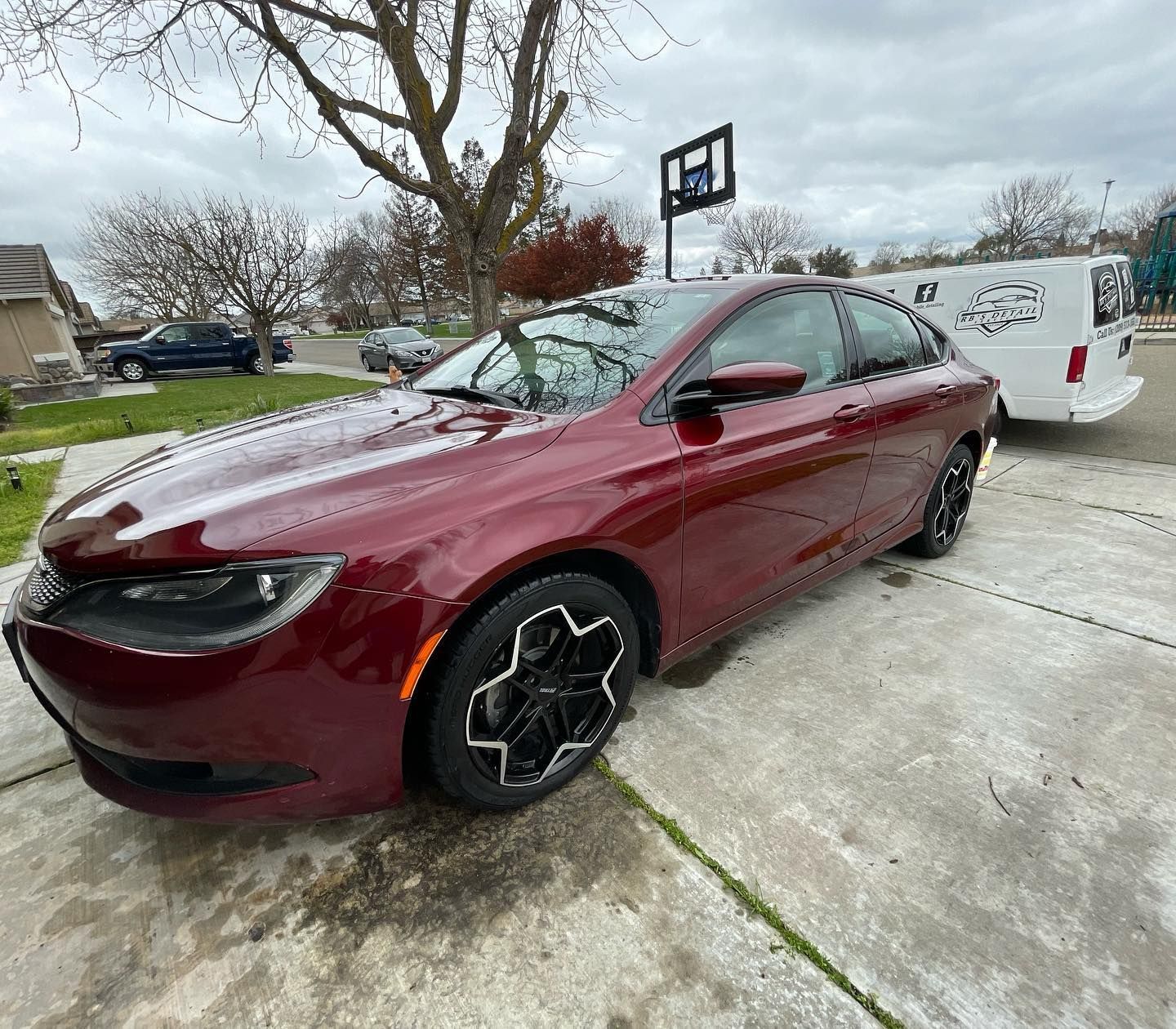 A red car is parked in a driveway next to a white van.