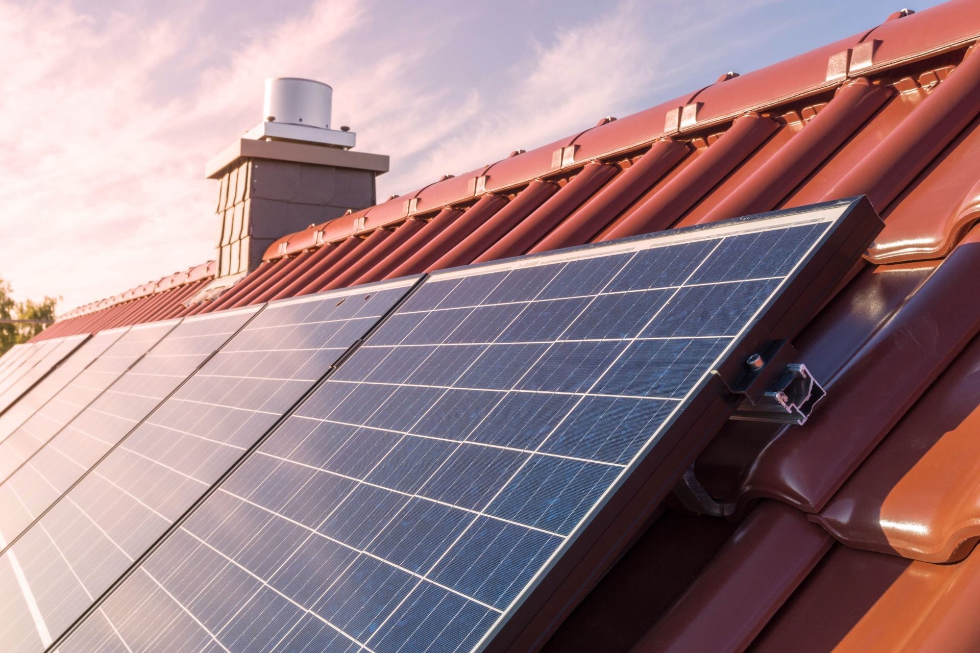 Solar panels installed on a red tile roof, chimney in the background.