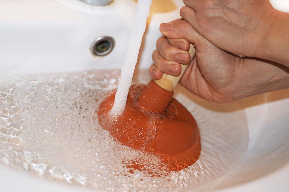 Woman With Plunger Trying To Unclog Blocked Drain