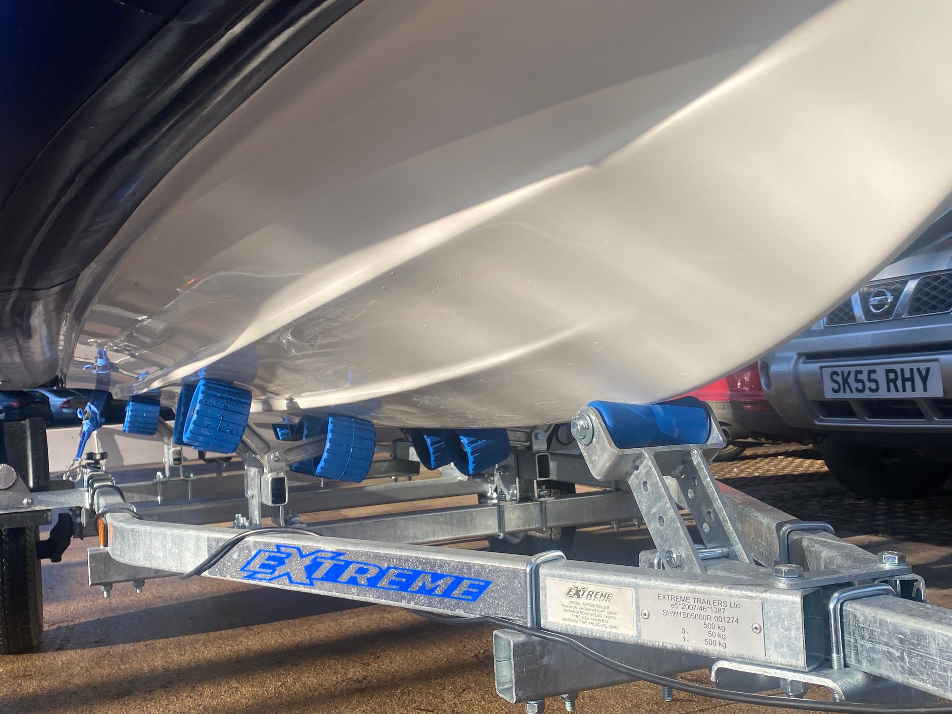 Boat hull resting on blue rollers of a silver Extreme trailer.