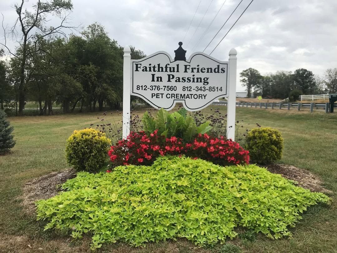 Faithful Friends Passing memorial sign with flowers and greenery in a grassy outdoor park.