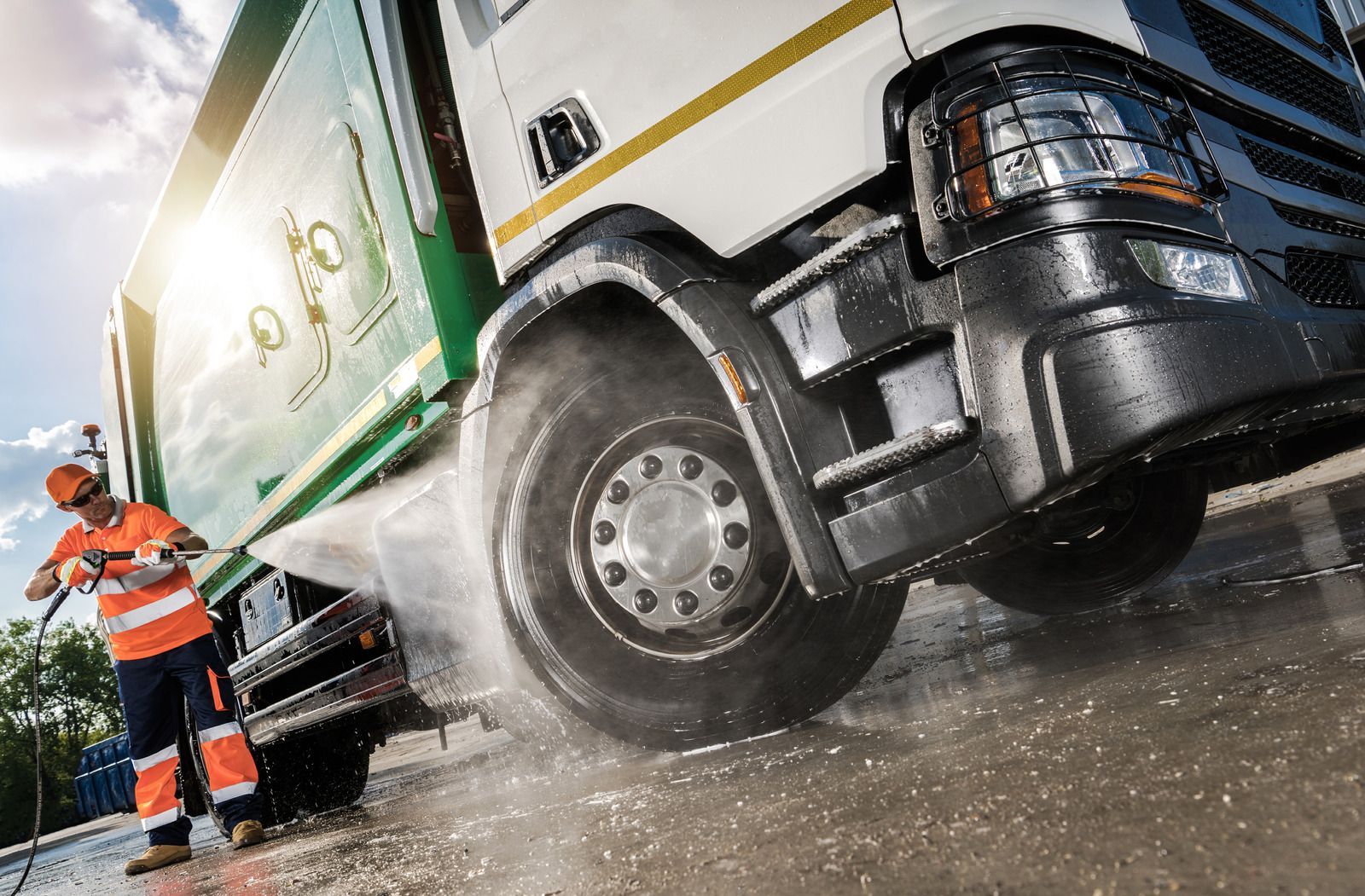 A man is washing a garbage truck with a high pressure washer.
