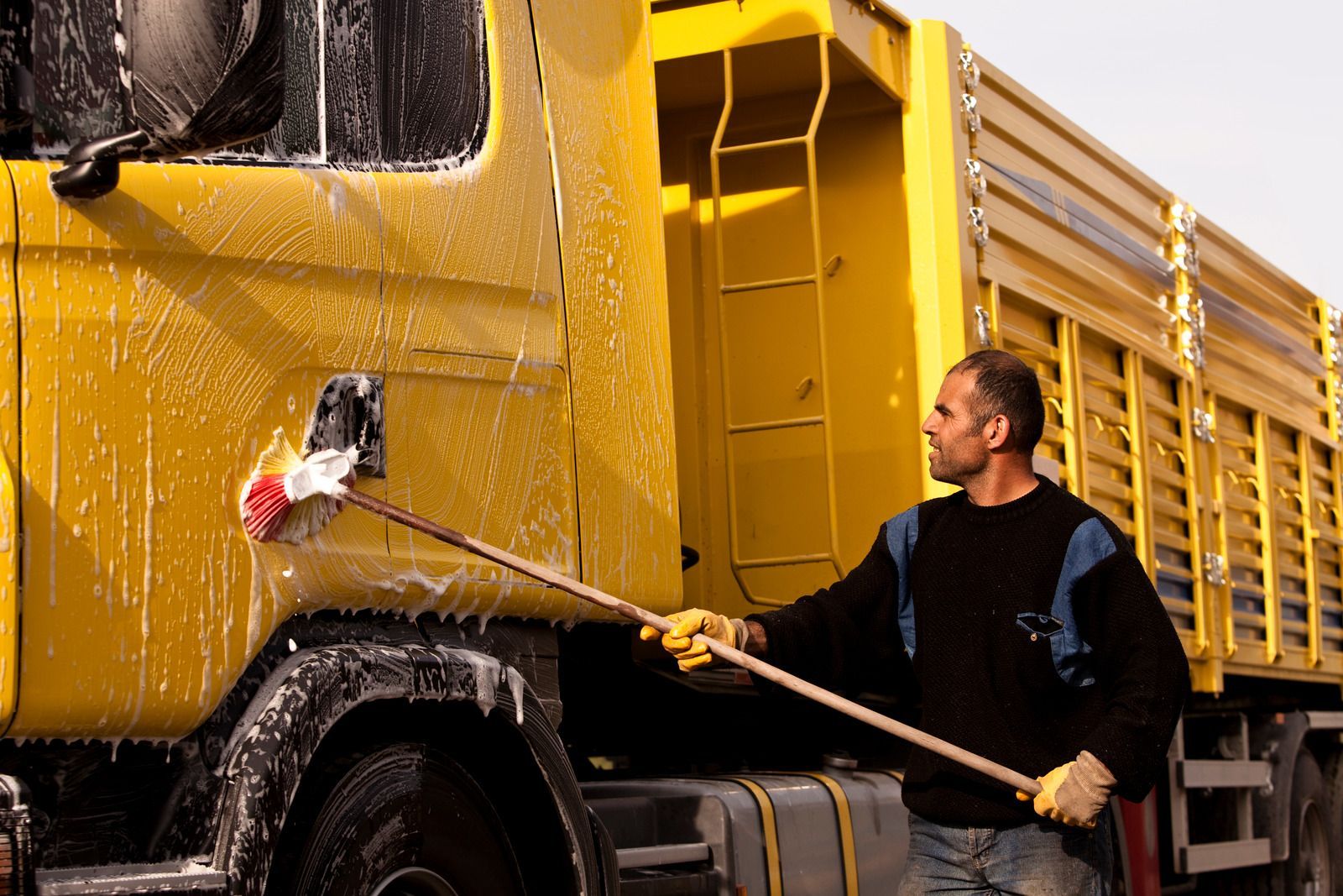 A man is washing a yellow truck with a broom